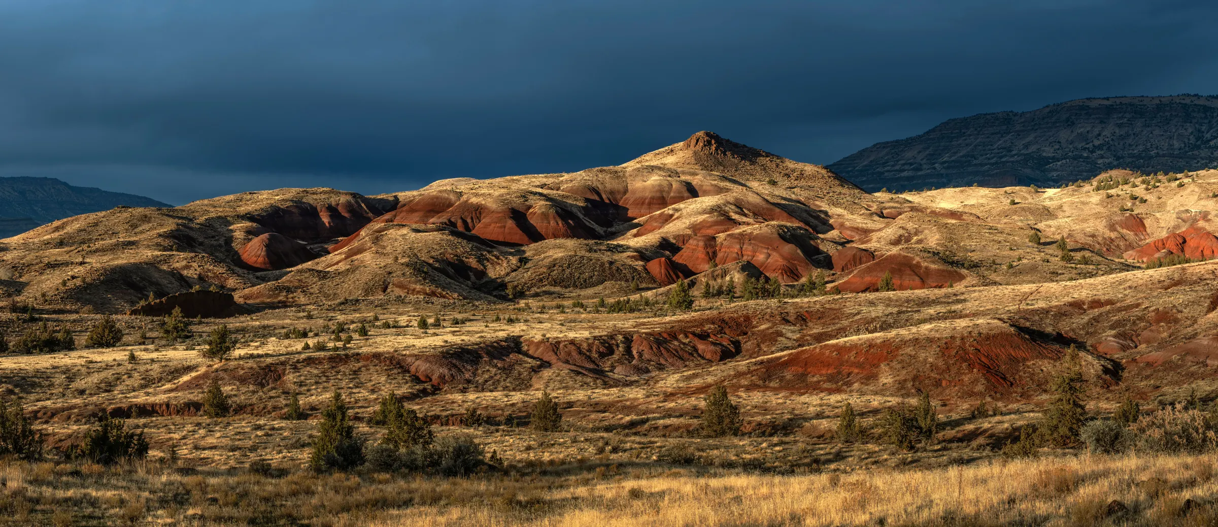 Collines rouges et ocre des Painted Hills sous un ciel d’orage sombre.