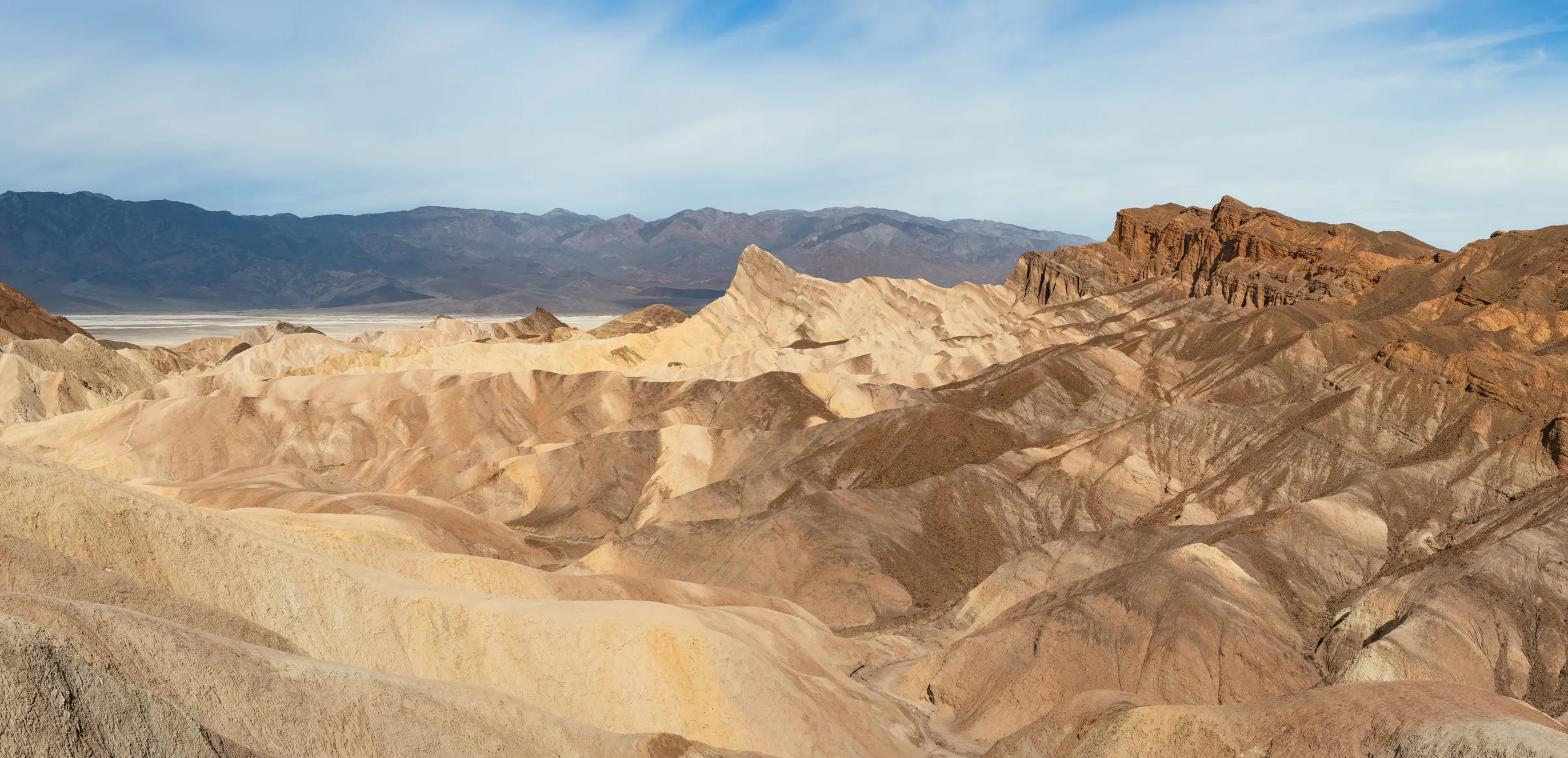 Badlands stratifiés de la Furnace Creek Formation vus depuis Zabriskie Point, ciel pâle à gauche, falaises rouges à droite.