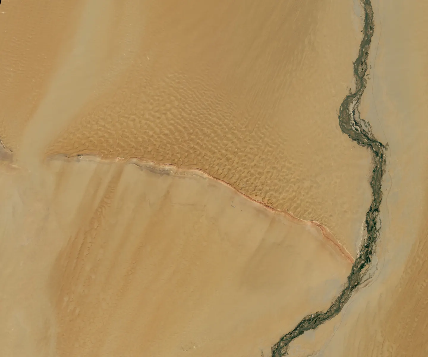 Landsat 9 satellite image of a red-and-white ridge crossing a sand desert, with a winding river.
