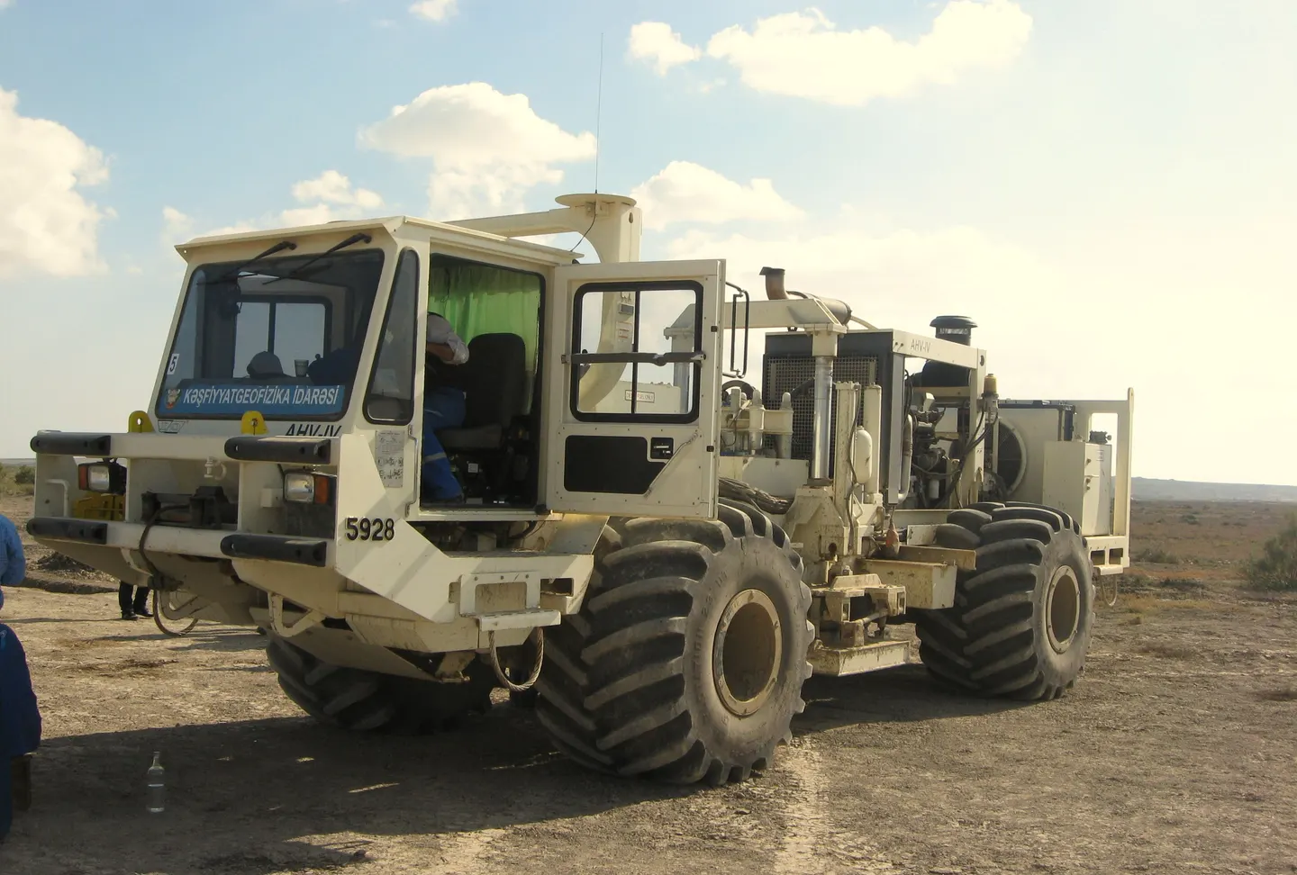 Land seismic vibrator truck on a dirt track under a clear sky.